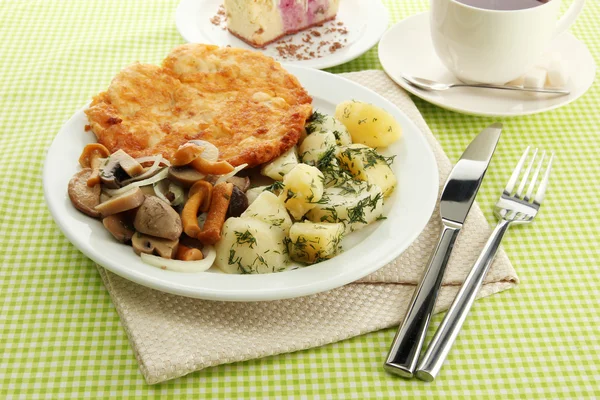Gebratenes Hühnerschnitzel mit gekochten Kartoffeln und Gemüse, Tasse Tee und Dessert, auf grünem Tischtuch — Stockfoto