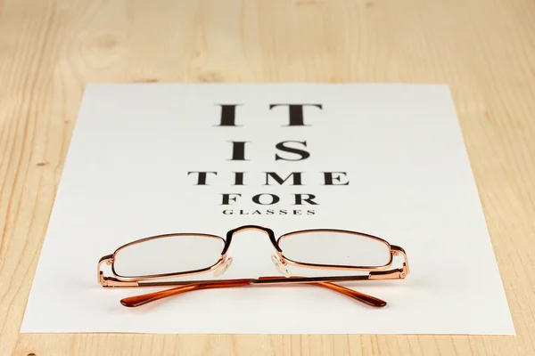 Eyesight test chart with glasses on wooden background close-up — Stock Photo, Image