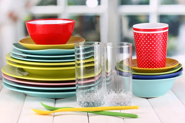 Colorful tableware on wooden table on window background — Stock Photo, Image