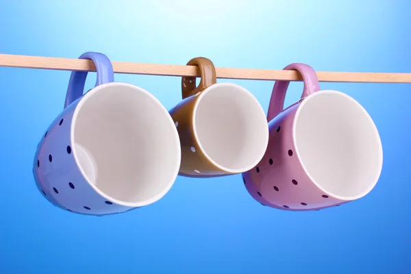 Nice cups hanging on stick on blue background — Stock Photo, Image