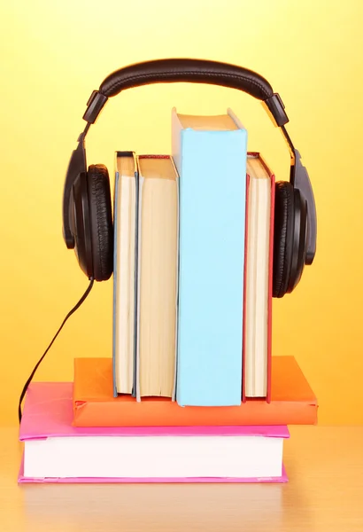 Kopfhörer auf Büchern auf Holztisch auf orangefarbenem Hintergrund — Stockfoto