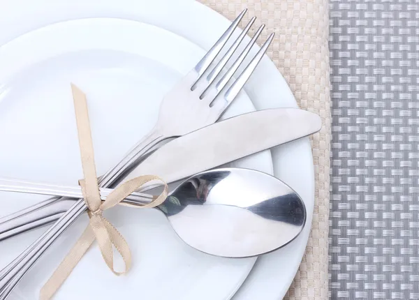 Plăci goale albe cu furculiță, lingură și cuțit legate cu o panglică pe o față de masă gri — Fotografie, imagine de stoc
