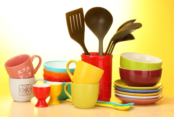 Heldere lege kommen, keukengerei op houten tafel op gele achtergrond en cups — Stockfoto