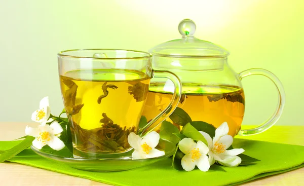 Green tea with jasmine in cup and teapot on wooden table on green background — Stock Photo, Image