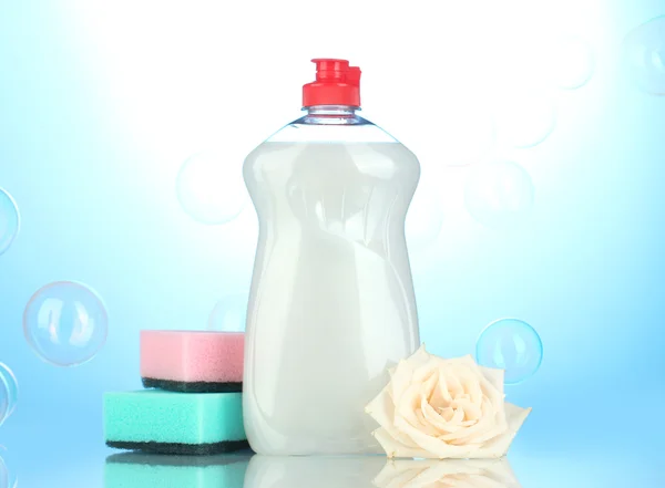 Líquido lavavajillas con esponjas y flores sobre fondo azul —  Fotos de Stock