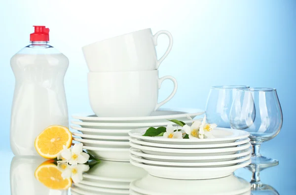 Prázdné čisté talíře, sklenice a kelímky s saponátů a citron na modrém pozadí — Stock fotografie
