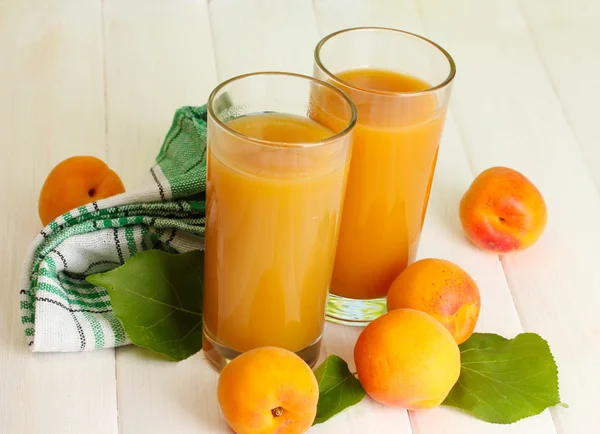 Glasses of apricot juice and fresh apricots on white wooden table — Stock Photo, Image