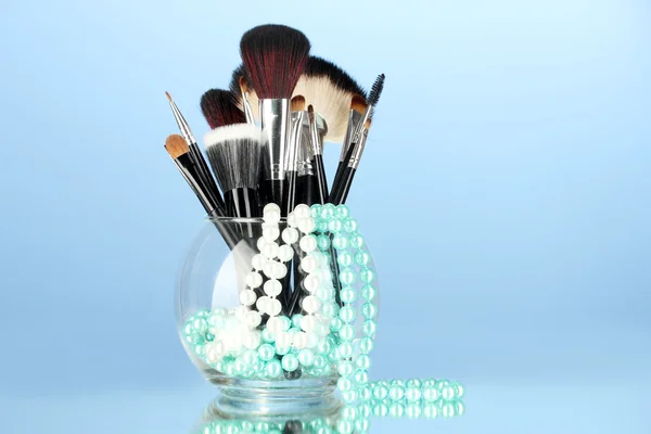 Cepillos de maquillaje en un tazón con collar de perlas sobre fondo azul — Foto de Stock