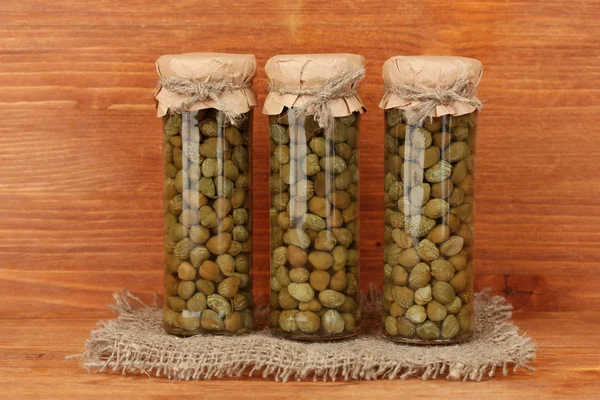 Glass jar with tinned capers on wooden background close-up — Stock Photo, Image
