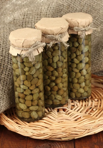 Glass jars with tinned capers on sack background close-up — 스톡 사진