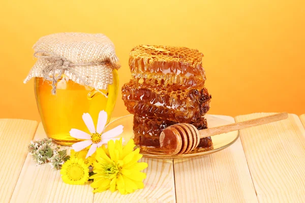 Frasco de mel e favo de mel na mesa de madeira no fundo laranja — Fotografia de Stock