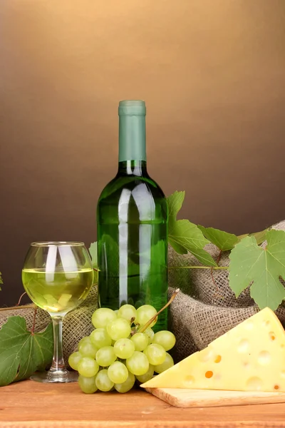 Láhev značkového vína se sklem a sýrem na dřevěný stůl na hnědé pozadí — Stock fotografie