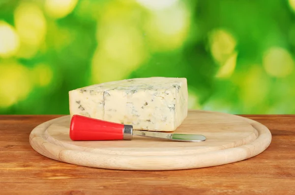 Cheese with mold and knife on the cutting board on bright green background — Stock Photo, Image