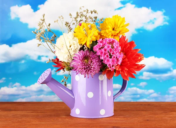 Purple watering can with white polka-dot with flowers on sky background — Stock Photo, Image