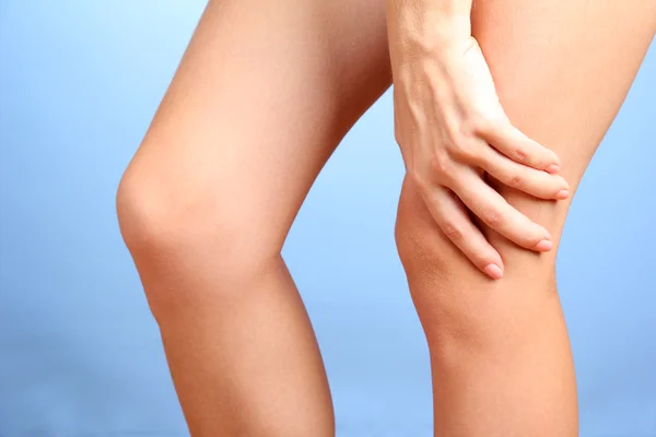 Woman holding sore knee, on blue background — Stock Photo, Image