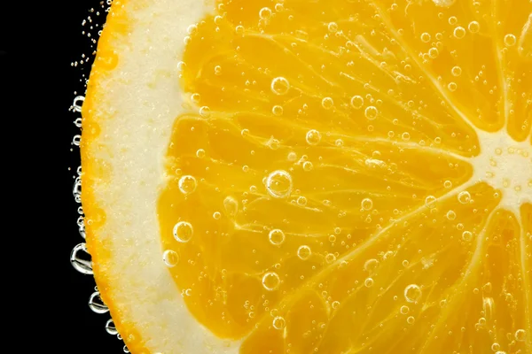 Fetta di arancia in acqua con bolle, su fondo nero — Foto Stock