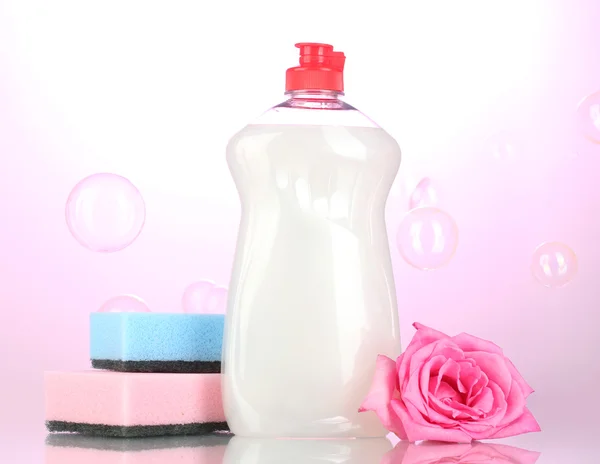 Жидкость для мытья посуды с губками и цветами на розовом фоне — стоковое фото