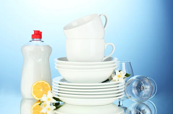 Piatti puliti vuoti, bicchieri e tazze con liquido per piatti e limone su sfondo blu — Foto Stock