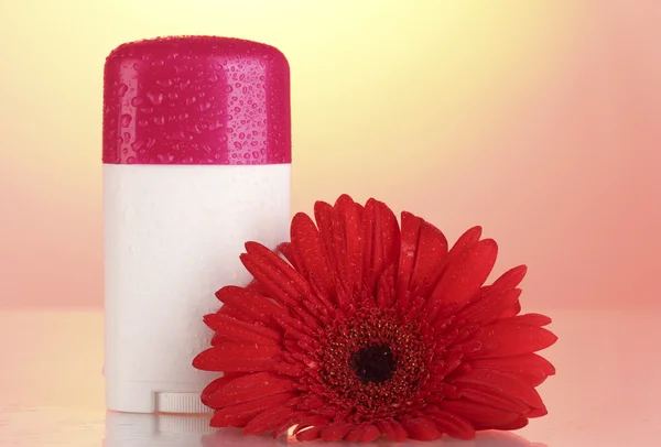 Deodorant with flower on red-yellow background — Stock Photo, Image