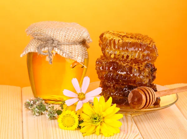 Frasco de mel e favo de mel na mesa de madeira no fundo laranja — Fotografia de Stock