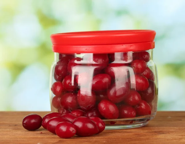 Fresh cornel berries in glass jar on green background close-up — Stock Photo, Image