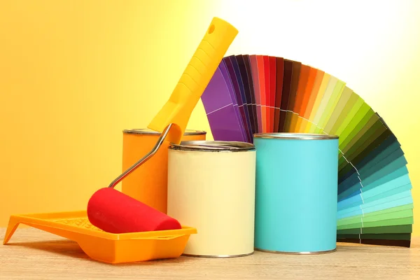 Blechdosen mit Farbe, Rolle, Pinsel und heller Farbpalette auf Holztisch auf gelbem Hintergrund — Stockfoto