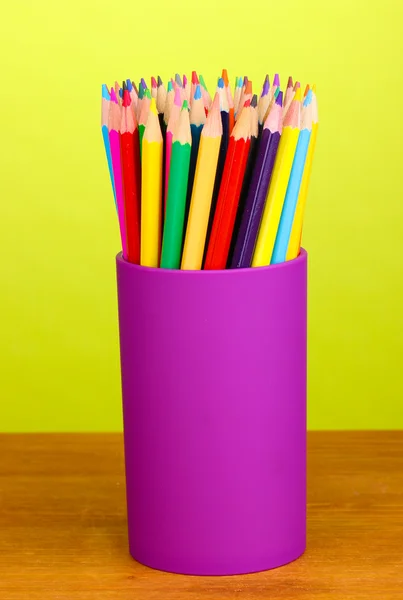 Color pencils in glass on wooden table on green background — Stock Photo, Image