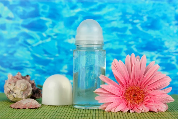 Дезодорант, цветок и раковины на синем фоне моря — стоковое фото
