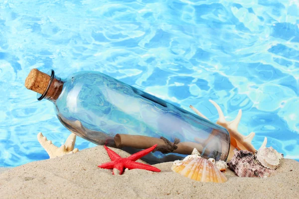 Garrafa de vidro com nota no interior na areia, no fundo azul do mar — Fotografia de Stock