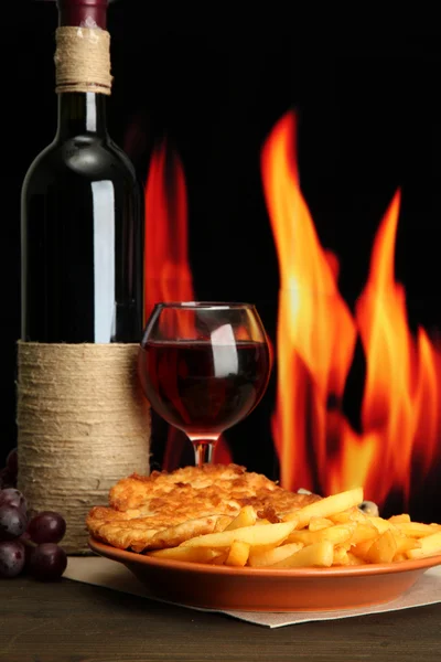 फ्रांसीसी फ्राइज़ के साथ भुना हुआ चिकन कटलेट, आग पृष्ठभूमि पर शराब का ग्लास — स्टॉक फ़ोटो, इमेज
