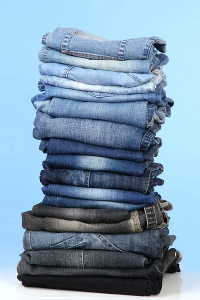 Muitas calças de ganga empilhadas em uma pilha no fundo azul — Fotografia de Stock