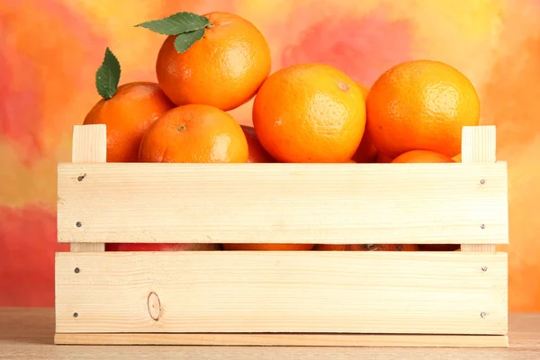 Ripe tasty tangerines with leaves in wooden box on table on orange background — Stock Photo, Image
