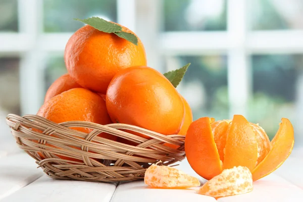 Tangeriner med blad i en vacker korg, på träbord på fönsterbakgrund — Stockfoto