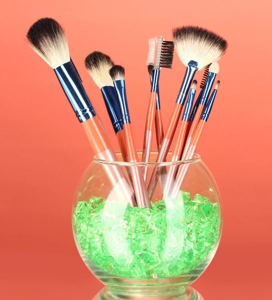 Make-up brushes in a bowl with stones on red background — Stock Photo, Image