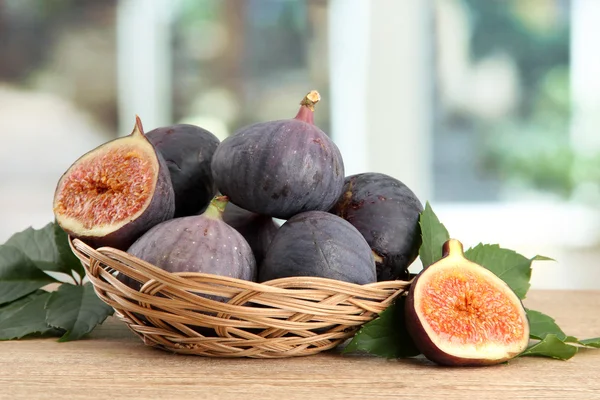 Ripe sweet figs with leaves in basket, on wooden table, on window background — Stock Photo, Image