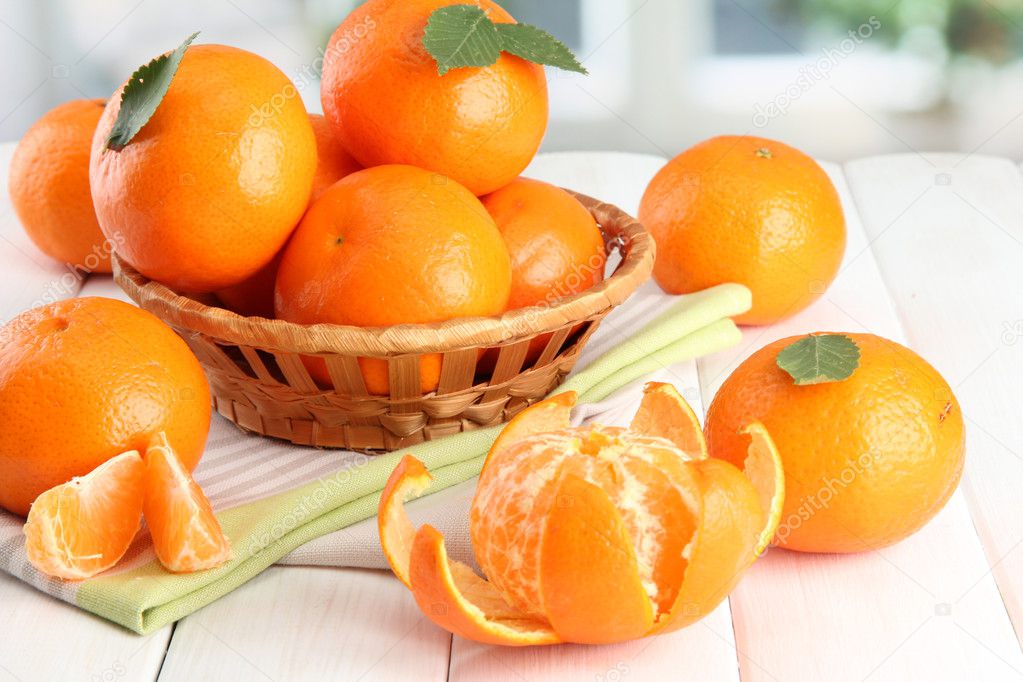 Tangerines with leaves in a beautiful basket, on white wooden table
