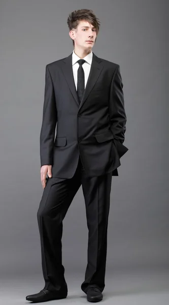 Mladý podnikatel černý oblek ležérní kravatu na šedém pozadí — Stock fotografie