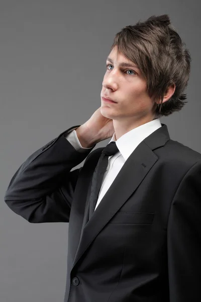 Mladý podnikatel černý oblek ležérní kravatu na šedém pozadí — Stock fotografie