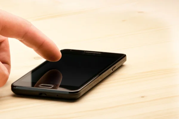 Mans hand vidrör skärmen av svart smartphone på trä skrivbord — Stockfoto