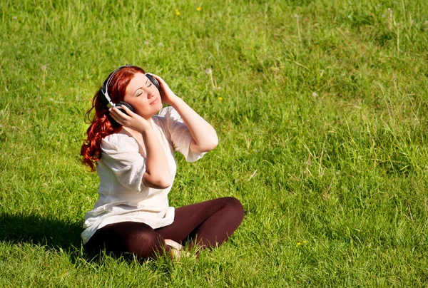 Linda ruiva jovem ouvindo música com fones de ouvido — Fotografia de Stock
