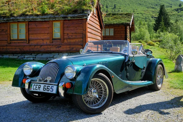 stock image Old-fashioned car against the wood houses in mountain forest.