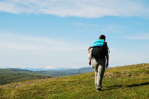 Woman hiking between green hills and the blue sky. — Stock Photo, Image