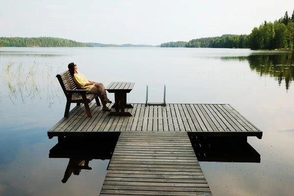 Lake with wooden platform and woman resting. — Stock Photo, Image