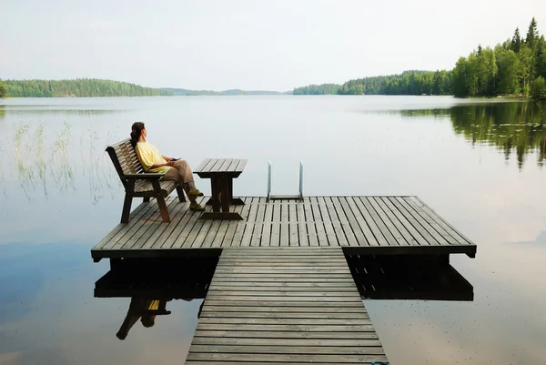 Lago con plataforma de madera y mujer descansando . —  Fotos de Stock
