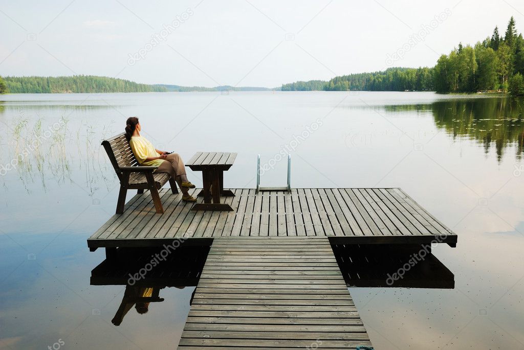 Lake with wooden platform and woman resting.