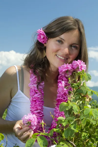 Schönes, glückliches Mädchen, das eine Rose riecht und eine Girlande aus Rosen trägt — Stockfoto
