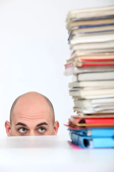 Man hiding behind a desk watching a stack of books — Stock Photo, Image