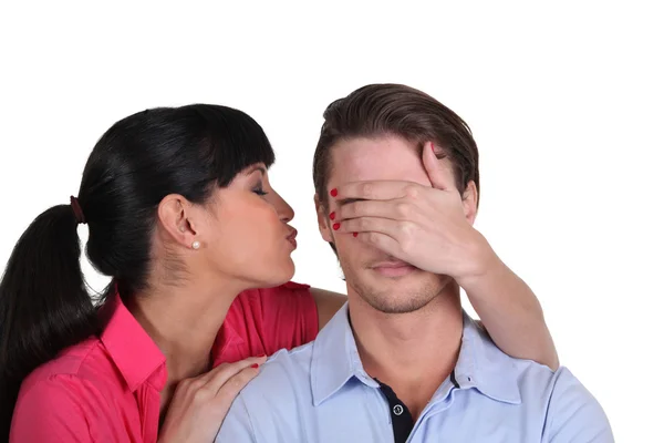 Jovem mulher beijando seu namorado na bochecha escondendo seus olhos — Fotografia de Stock