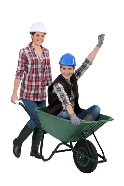 Hantverkerska bär en kollega som sitter i en skottkärra — Stockfoto