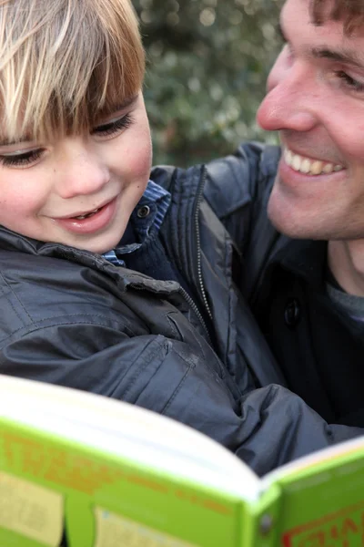 Отец и сын читают книгу на открытом воздухе — стоковое фото